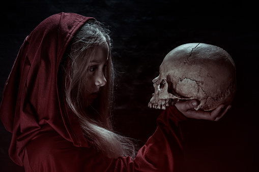 Portrait of young Witch holding human skull