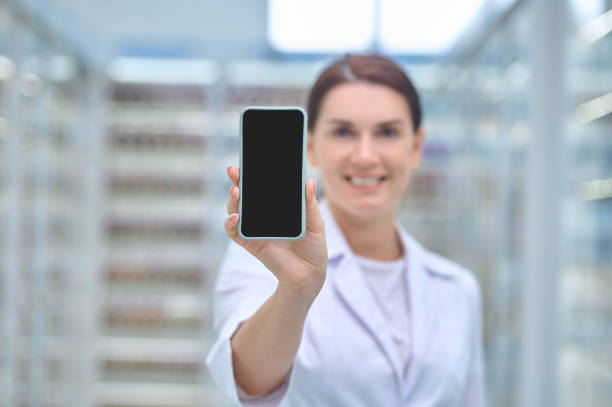 Woman in medical gown showing smartphone screen stock photo