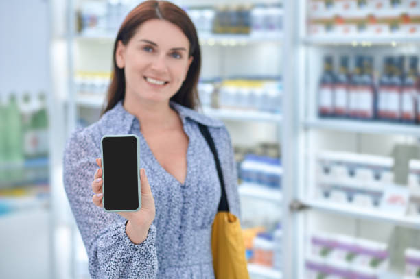 Joyful woman showing smartphone screen in pharmacy stock photo