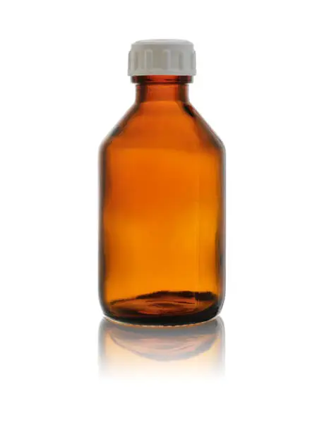 Photo of An empty medical bottle made of brown glass, closed with a lid. Isolated on a white background with reflection