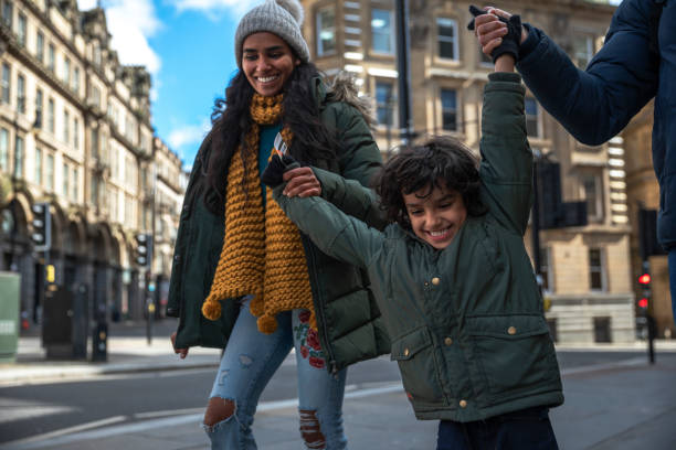 Swings in the City A multiracial family of three, a mother, father and their little boy on a staycation in the city of Newcastle on a sunny winters day. They are wearing casual, winter clothing and accessories. They are walking down a city street, holding hands and swinging their little boy in the air. day in the life stock pictures, royalty-free photos & images