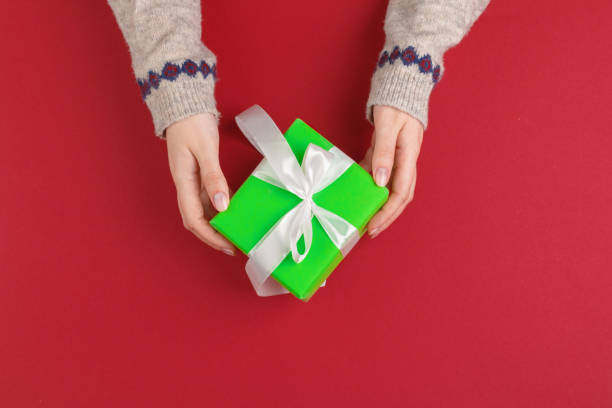 istock Female hands with christmas gift on red background, top view, copy space 1346386231
