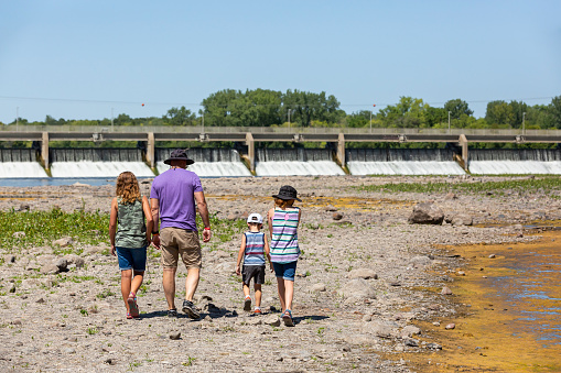 Father with three children walking on a dry river bed during a drought. Normally this land would be covered with water from the Mississippi River, which can be seen flowing through a dam in the distance.