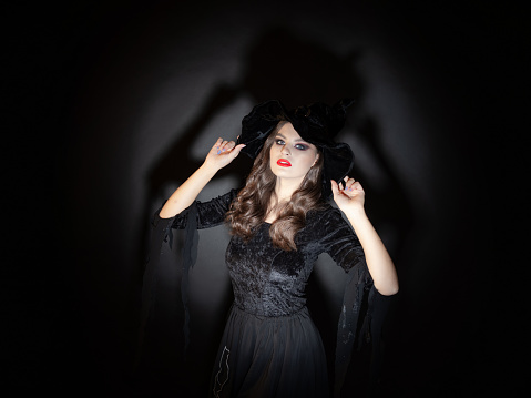 witch at Halloween party, a young beautiful brunette woman in a classic witch costume with a pointed hat. Caught off guard in the spotlight, a witch is discovered.