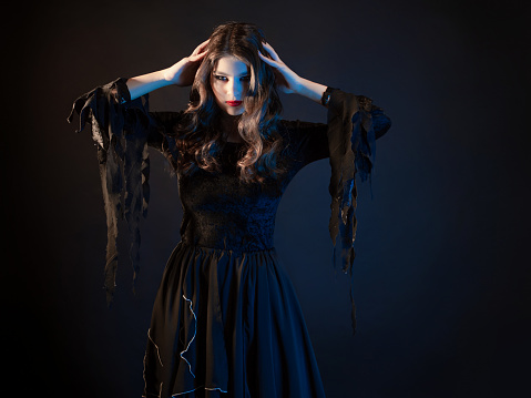 A beautiful young woman in a witch dress, a beautiful and gloomy image for Halloween, photo on black