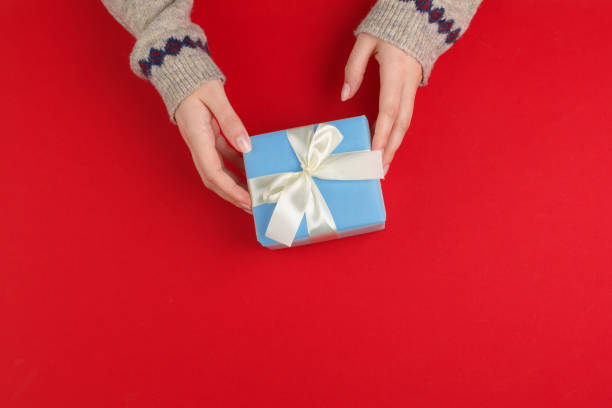 istock Female hands with christmas gift on red background, top view, copy space 1346390213