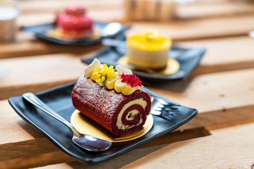Delicious Chocolate flavor swiss roll, orange cheesecake, strawberry oat cheesecake served with black ceramic plate on wooden table.