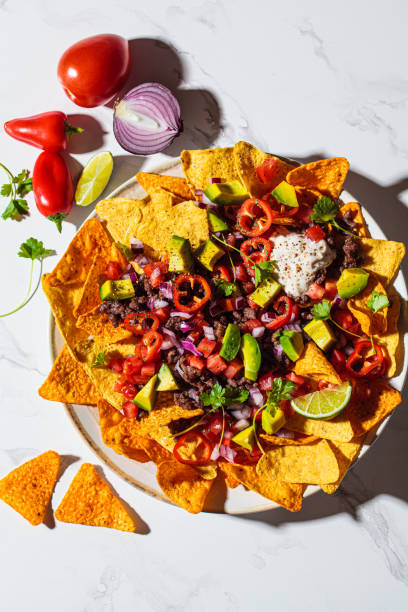 istock Mexican food concept. Corn nachos chips with avocado, pepper, salsa and grilled minced beef on white plate, white marble background. 1346391736