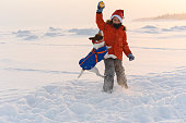 Boy wearing warm clothing and Santa Claus hat playing with his pet dog on a beach of White sea on December day