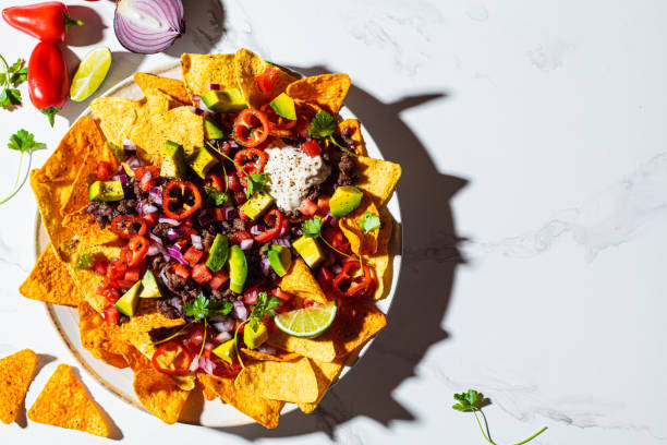 istock Mexican food concept. Corn nachos chips with avocado, pepper, salsa and grilled minced beef on white plate, white marble background. 1346391790