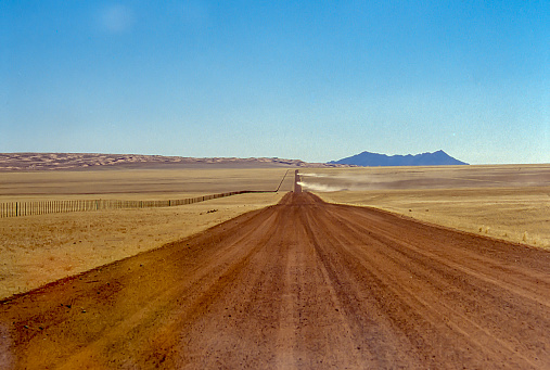 The dirt track stretches straight to the horizon in the arid plains of Namibia.