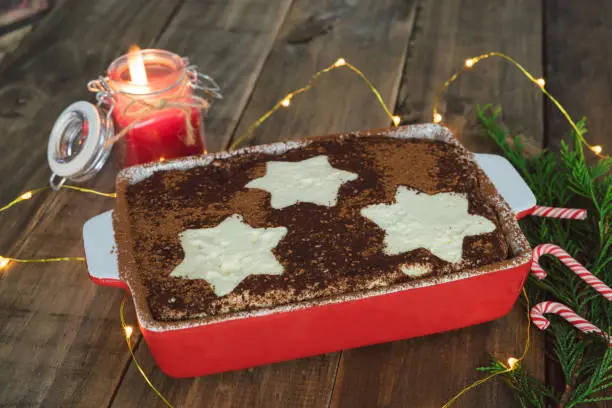 Tiramisu traditional Italian dessert with Christmas decoration and candle lit with Christmas lights. Copy space.