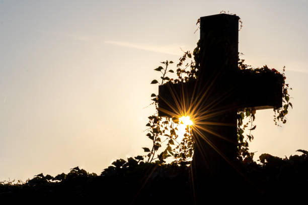 Glowing cross silhouette with sunbeams sunset sunlight and clear evening sky shows christianity spirituality of church and forgiveness at grave and death for catholic resurrection metaphors on easter Glowing cross silhouette with sunbeams sunset sunlight and clear evening sky shows christianity spirituality of church and forgiveness at grave and death for catholic resurrection metaphors on easter grave digger stock pictures, royalty-free photos & images