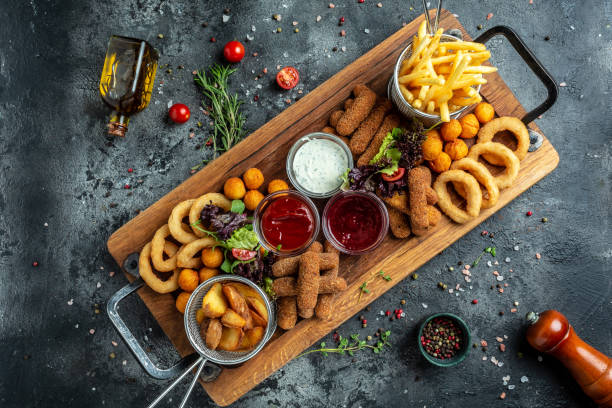 fast food meals mozzarella sticks, onion rings, french fries, chicken nuggets and sauce. pub appetizers on a wooden board. banner, menu, recipe place for text, top view stock photo