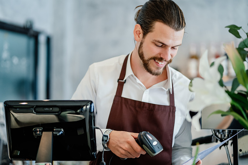 Barista young man scanning QR code or barcode in menu paper at counter in cafeteria. New payment technology concept.