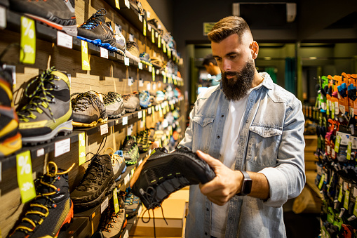 Adventurous male customer enjoying outdoor equipment shopping and choosing the perfect hiking shoes for new adventures in the mountains.