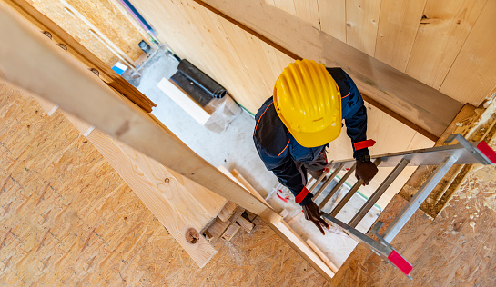 Man construction worker builder on ladder wearing yellow helmet on interior site building background
