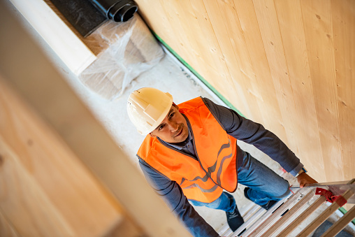 Man construction worker builder on ladder wearing yellow helmet on interior site building background