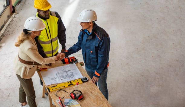 gruppo di architetti che correggono un piano di costruzione in cantiere - indoors blueprint smiling built structure foto e immagini stock