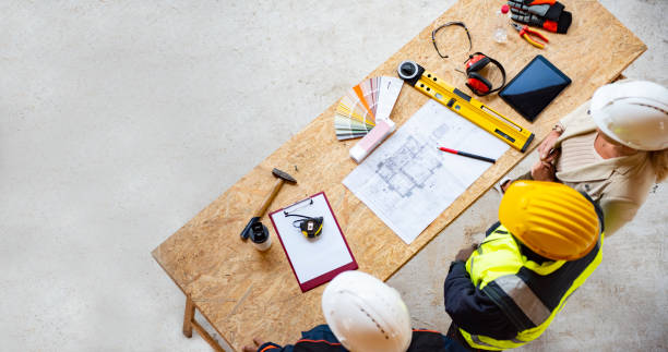 Group of architects correcting a construction plan at construction site Team of one women architect and two men architects on a construction site. They are looking at blueprint. They are discussing about their project. Shot from above. building contractor stock pictures, royalty-free photos & images