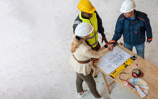 Team of one women architect and two men architects on a construction site. They are looking at blueprint. They are discussing about their project. Shot from above.