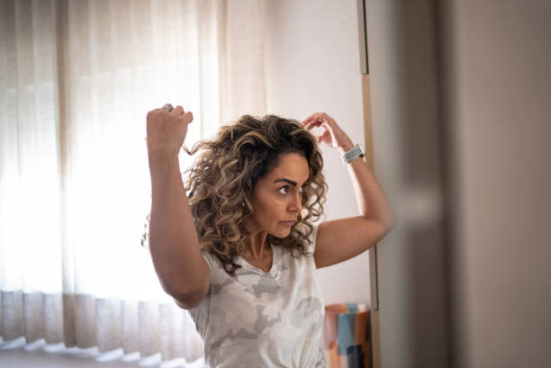 mature woman looking in the mirror styling her hair at home - mirror vanity women looking imagens e fotografias de stock