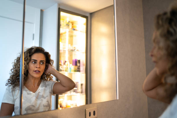 Mature woman looking in the mirror styling her hair at home