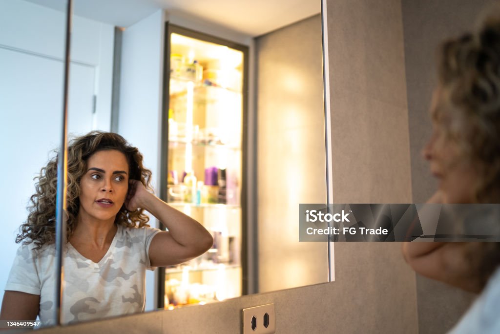 Mature woman looking in the mirror styling her hair at home Mirror - Object Stock Photo