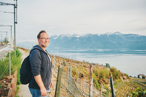 Middle age man hiking with backpack, posing next to railways with lake Geneva and Haute-Savoie view, Lavaux, Switzerland