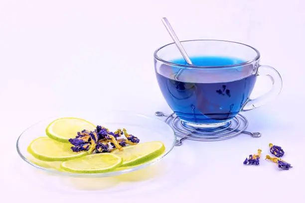 Photo of Cup of Butterfly pea tea with slice of lime. Cup of Anchan tea with dry flowers of Clitoria