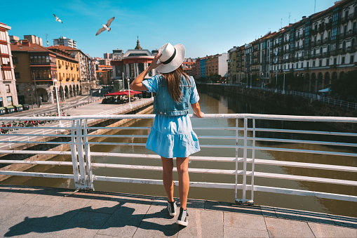 Rear view of young tourist woman in white sun hat walking in Bilbao city. Summer holiday vacation in Spain