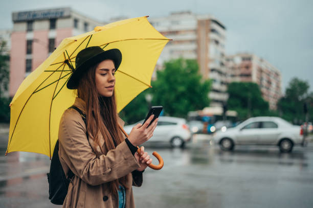 istock Woman using smartphone and holding yellow umbrella while in the city while it rains 1346428628