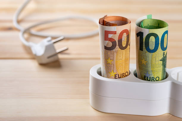 istock Euro money banknotes inserted into a white extension socket on a wooden surface. Increasing of electricity cost. 1346431152