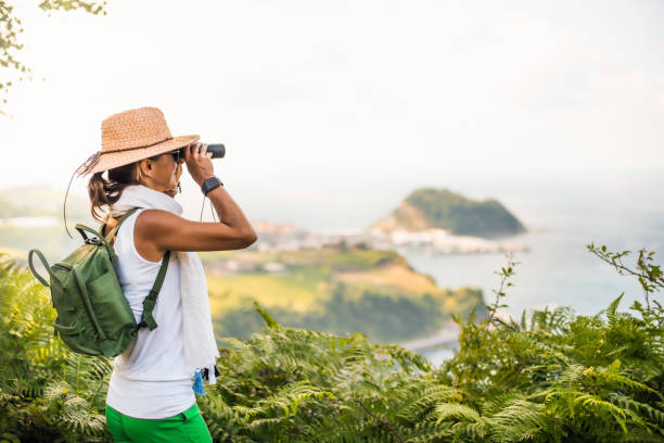 istock a woman with a backpack and hat, observes the landscape with a pair of binoculars. 1346433792