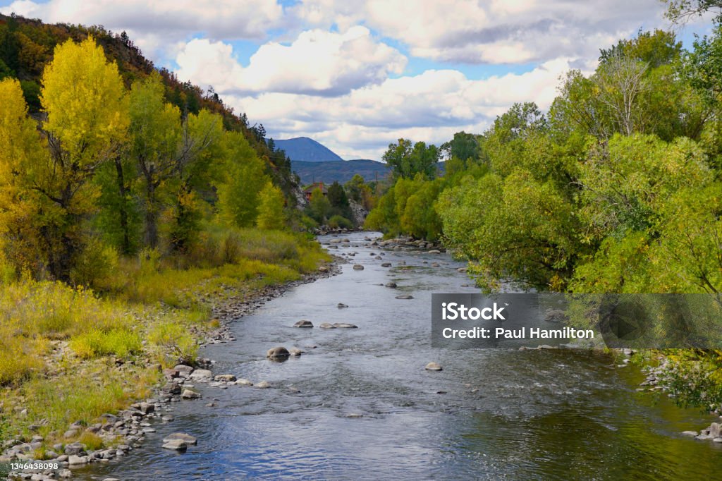 Yampa River flowing through Steamboat Springs Colorado Section of the Yampa river lined by trees with autumn colors under a sky filled with clouds Steamboat Springs Stock Photo