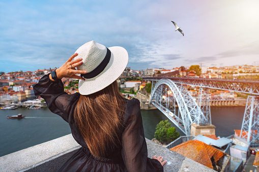 Young woman tourist enjoying beautiful view of Porto city and famous Dom Luis I Bridge at sunset. Summer holiday vacation in North Portugal. High quality photo