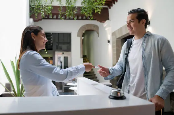 Happy man arriving at a hotel and doing the check-in at the front desk while receptionist gives him the keys of his room