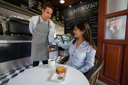 Happy Latin American woman making a contactless payment at a cafe with her cell phone - food and drinks concepts. **DESIGN ON MENU AND SCREEN BELONG TO US**