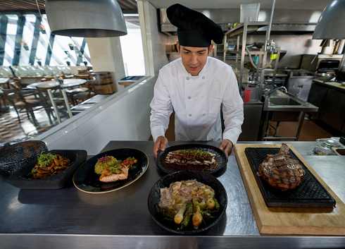 Latin American chef cooking in the kitchen of a restaurant and presenting his plates for service - food and drink concepts