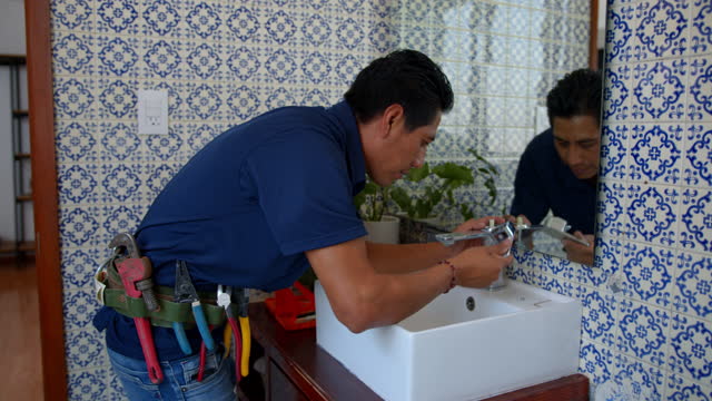 Latin American plumber fixing the bathroom’s sink faucet at a customers home