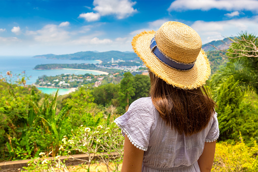 Woman traveler wearing blue dress and straw hat at   Panorama of Karon View Point at Phuket in Thailand in a summer day