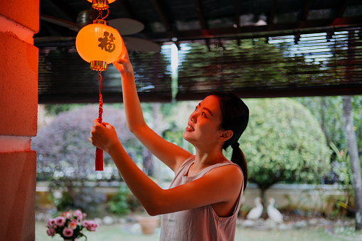 Image of an Asian Chinese woman hanging red lanterns and decorating house for Chinese New Year celebration
