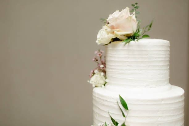 istock Two tiered white cake with fresh roses decoration on neutral beige background with copy space. 1346468812