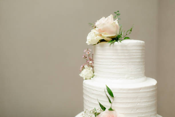 istock Two tiered white cake with fresh roses decoration on neutral beige background with copy space. 1346468821