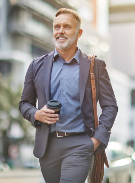 Shot of a handsome mature businessman walking around town drinking coffee I can feel the caffeine in my veins businessman happiness outdoors cheerful stock pictures, royalty-free photos & images