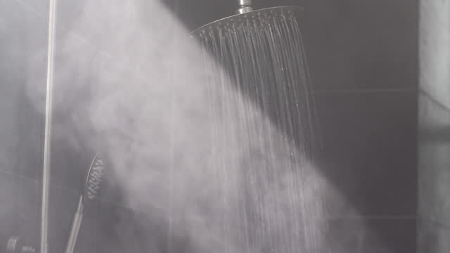 Warm water streams make hot vapor in grey tiled shower
