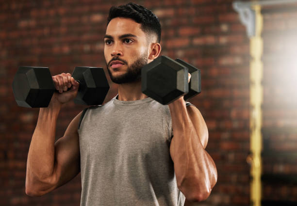 Shot of a young man working out with dumbbells in a gym The longer you hold, the stronger you get LIFTING WEIGHTS stock pictures, royalty-free photos & images