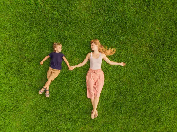 Photo of Mom and son are lying on the grass in the park, photos from the drone, quadracopter