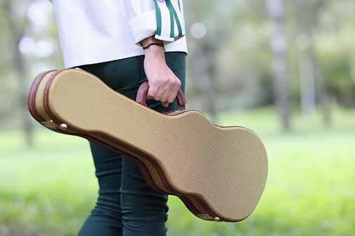 Woman holds violin and guitar case and walks through park. Street musicians and loneliness concept