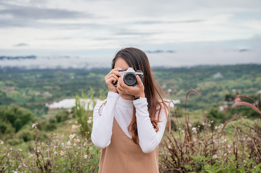 Attractive asian woman taking photo with retro film camera among the nature at countryside in the morning